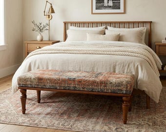 May include: A bedroom scene featuring a wooden bed frame with neutral-colored bedding and a patterned bench at the foot. A framed black and white photo hangs above the bed. The rug and bench have a similar color palette of rust, beige, and black.