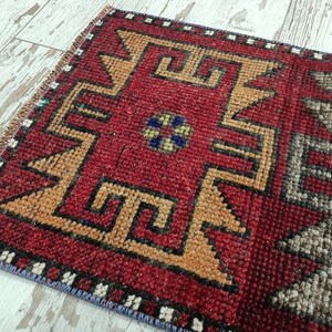May include: A red, orange, black, and gray patterned rug with a geometric design. The rug has a fringe border.
