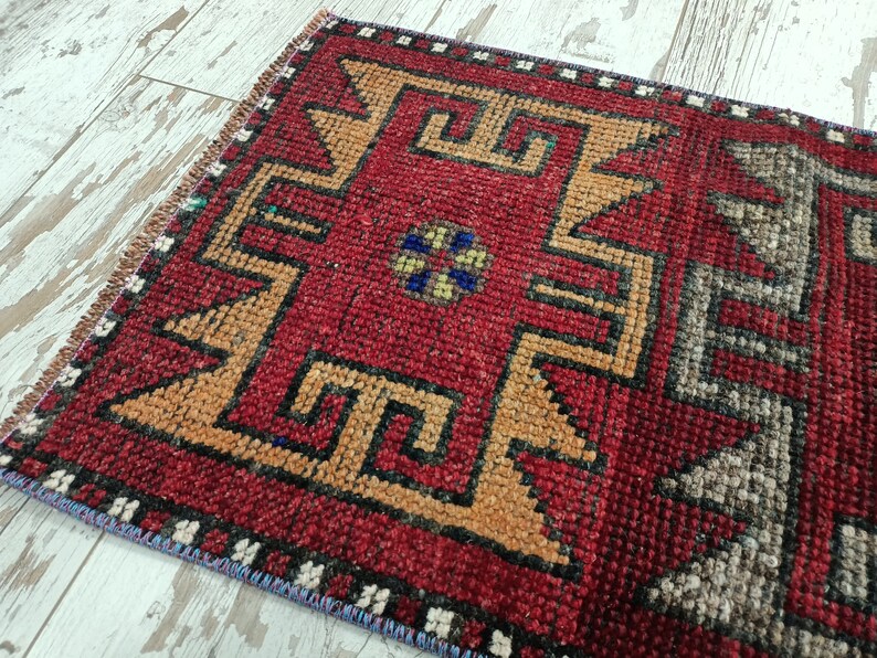 May include: A red, orange, black, and gray patterned rug with a geometric design. The rug has a fringe border.