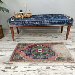 Peut inclure: Un banc bleu et rose &agrave; motifs avec des pieds en bois est pos&eacute; sur un sol en bois blanchi &agrave; la chaux. Un petit tapis &agrave; motifs g&eacute;om&eacute;triques verts, roses et bleus se trouve devant le banc.