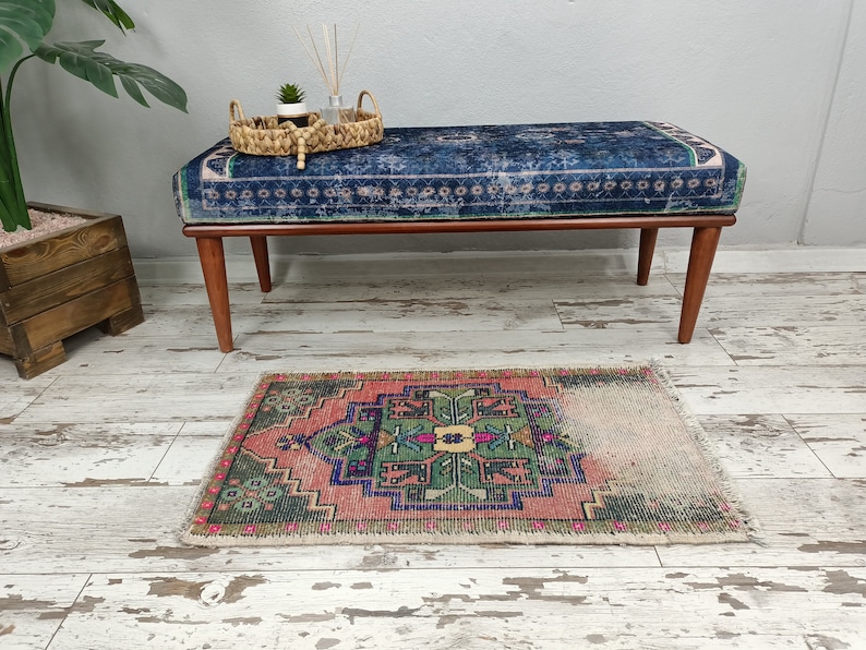 Peut inclure: Un banc bleu et rose &agrave; motifs avec des pieds en bois est pos&eacute; sur un sol en bois blanchi &agrave; la chaux. Un petit tapis &agrave; motifs g&eacute;om&eacute;triques verts, roses et bleus se trouve devant le banc.