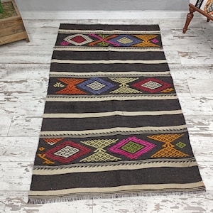 May include: A black and white rug with colorful geometric patterns. The rug has a fringe border and is made of wool.