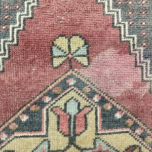 May include: Close-up of a vintage rug with a red background and intricate geometric patterns in shades of blue, beige, and cream. The rug features a central design with a stylized flower motif.