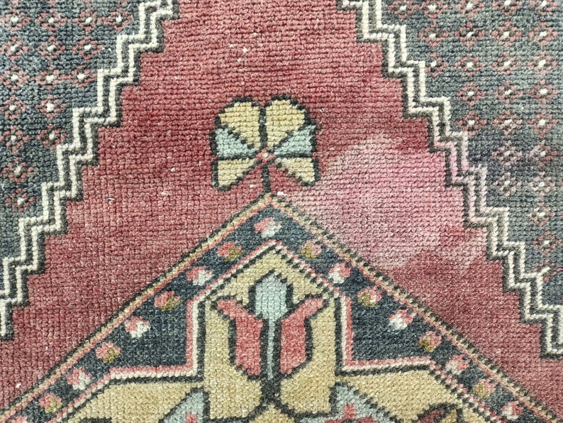 May include: Close-up of a vintage rug with a red background and intricate geometric patterns in shades of blue, beige, and cream. The rug features a central design with a stylized flower motif.