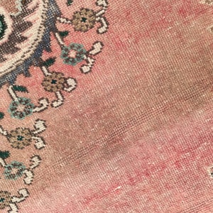 May include: Close-up of a pink and blue patterned rug with a faded, worn look. The rug has a floral design with intricate details.