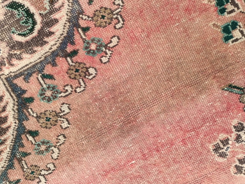 May include: Close-up of a pink and blue patterned rug with a faded, worn look. The rug has a floral design with intricate details.