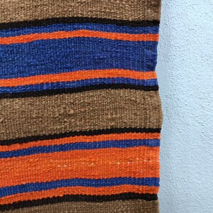 May include: A woven rug with brown, orange, and blue stripes. The rug is made of a thick, textured fabric.