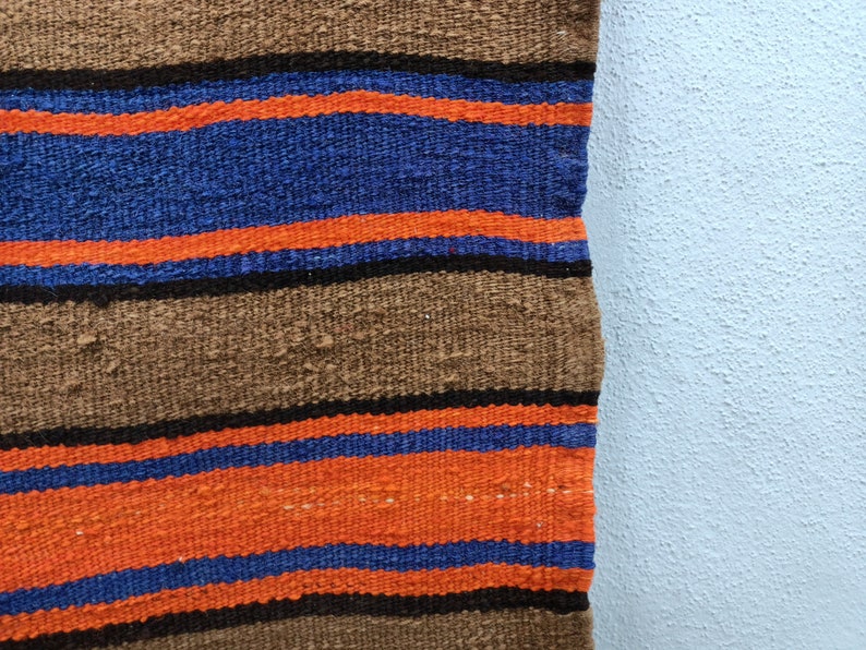 May include: A woven rug with brown, orange, and blue stripes. The rug is made of a thick, textured fabric.