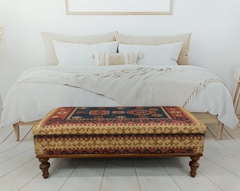 May include: A rectangular storage ottoman with a dark wood frame and legs. The top is upholstered in a colorful patterned fabric with red, blue, and beige tones.