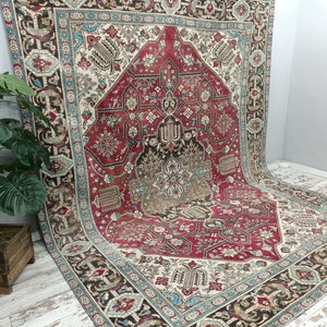 May include: A large, intricately patterned rug with a red, cream, and blue color scheme. The rug has a central medallion with a floral design and a border with geometric patterns.