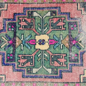 Peut inclure: Un tapis vintage avec un motif g&eacute;om&eacute;trique dans des tons de rose, vert, bleu et noir. Le tapis a un aspect us&eacute; et vieilli, ce qui ajoute &agrave; son charme.