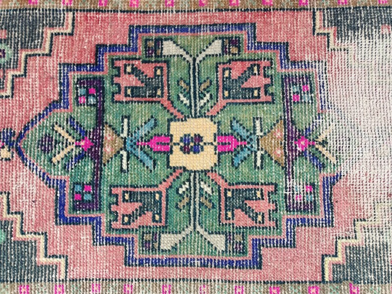Peut inclure: Un tapis vintage avec un motif g&eacute;om&eacute;trique dans des tons de rose, vert, bleu et noir. Le tapis a un aspect us&eacute; et vieilli, ce qui ajoute &agrave; son charme.
