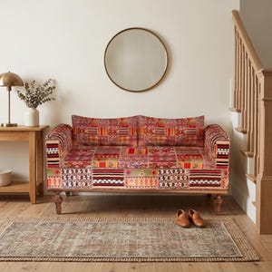 May include: A two-seater sofa with a patchwork design in shades of red, orange, and beige. The sofa has wooden legs and armrests. A round mirror hangs on the wall above the sofa.
