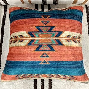 K&ouml;nnte beinhalten: Ein dekoratives Kissen mit einem s&uuml;dwestlich inspirierten Design. Das Kissen zeigt ein geometrisches Muster in Rot-, Orange-, Blau- und Wei&szlig;t&ouml;nen.