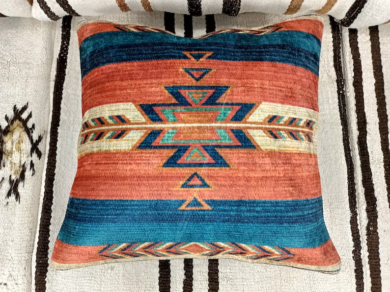 K&ouml;nnte beinhalten: Ein dekoratives Kissen mit einem s&uuml;dwestlich inspirierten Design. Das Kissen zeigt ein geometrisches Muster in Rot-, Orange-, Blau- und Wei&szlig;t&ouml;nen.