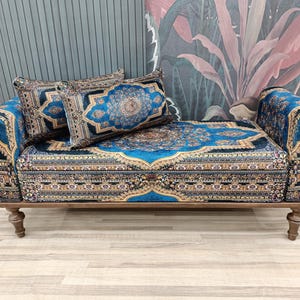 May include: A decorative loveseat with a detailed blue and gold patterned fabric. The loveseat has a wooden frame and legs, and includes two matching throw pillows. The design features a central medallion and ornate borders.