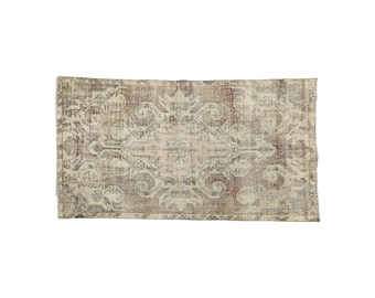 Puede incluir: Una alfombra vintage con un patrón intrincado descolorido en tonos marrones, beige y verdes. La alfombra tiene un aspecto desgastado y un borde con flecos.