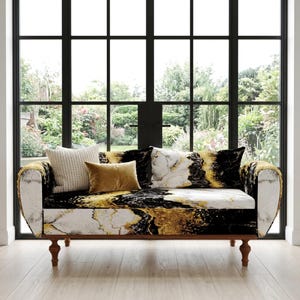 May include: A decorative sofa with a marble-like pattern in black, gold, and white. The sofa has a wooden frame and four legs. It is adorned with three throw pillows in cream, gold, and marble patterns. The sofa is placed in front of a large window.