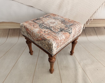 Könnte beinhalten: Ein kleiner, quadratischer Hocker mit einer gemusterten Stoffoberfläche und vier Holzbeinen. Der Stoff ist eine Mischung aus Beige, Orange und Schwarz.
