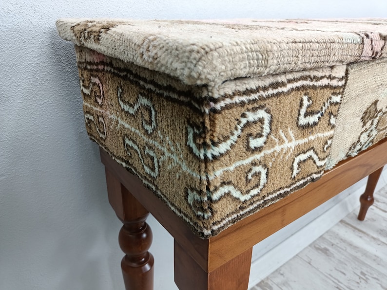 Op de afbeelding: Een houten kruk met een beige en bruin gepatroneerd stoffen bovenblad. De kruk heeft gedraaide houten poten.