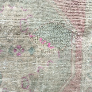 May include: Close-up of a beige rug with a faded pink and blue floral pattern. The rug has a worn and distressed look, with some areas showing signs of wear and tear.