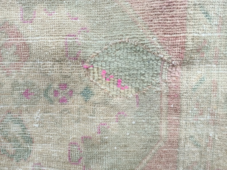 May include: Close-up of a beige rug with a faded pink and blue floral pattern. The rug has a worn and distressed look, with some areas showing signs of wear and tear.