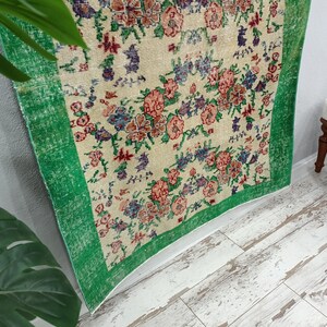 May include: A vintage rug with a floral pattern in shades of pink, red, blue, and green. The rug has a green border and is made of a soft, woven material.