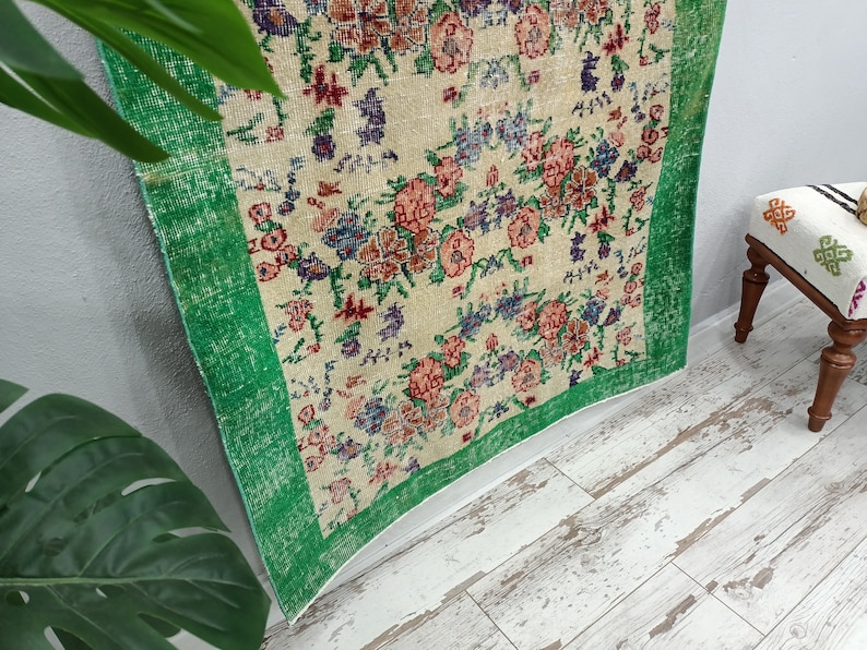 May include: A vintage rug with a floral pattern in shades of pink, red, blue, and green. The rug has a green border and is made of a soft, woven material.