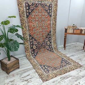 May include: A vintage rug with a floral pattern in shades of red, orange, blue, and cream. The rug has a fringed edge and is laid out on a whitewashed wooden floor.