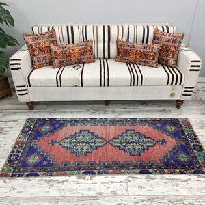 May include: A red and blue patterned rug with a white background. The rug is placed in front of a white couch with striped cushions.