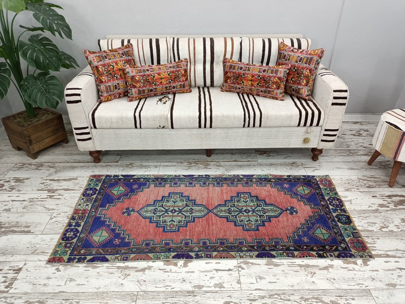 May include: A red and blue patterned rug with a white background. The rug is placed in front of a white couch with striped cushions.