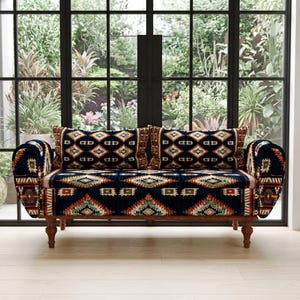 Può includere: Un divano blu navy con un motivo geometrico arancione, verde e bianco. Il divano ha due cuscini abbinati e gambe in legno. Il divano è di fronte a una grande finestra con vista su un giardino.