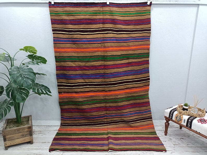 May include: A colorful striped rug with a brown background. The rug has stripes of red, orange, green, blue, and purple. The rug is hanging on a wall.