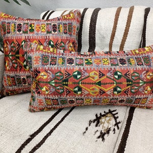 May include: Two decorative throw pillows with a colorful geometric pattern in shades of red, orange, yellow, green, blue, and black. The pillows are on a white and brown striped couch.