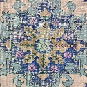 K&ouml;nnte beinhalten: Nahaufnahme eines Vintage-Teppichs mit einem blauen, gr&uuml;nen und rosafarbenen Blumenmuster. Der Teppich hat einen hellbeigen Hintergrund und ist mit komplizierten Details gewebt.