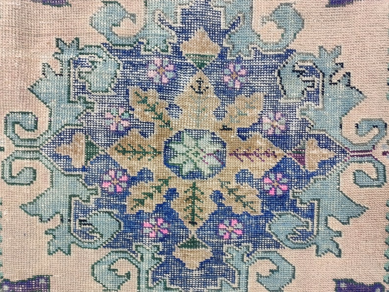 K&ouml;nnte beinhalten: Nahaufnahme eines Vintage-Teppichs mit einem blauen, gr&uuml;nen und rosafarbenen Blumenmuster. Der Teppich hat einen hellbeigen Hintergrund und ist mit komplizierten Details gewebt.