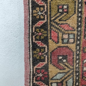 May include: Close-up of a colorful rug with intricate patterns in shades of red, gold, and black. The rug has a fringed edge and is woven with a detailed design.