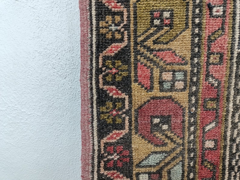 May include: Close-up of a colorful rug with intricate patterns in shades of red, gold, and black. The rug has a fringed edge and is woven with a detailed design.