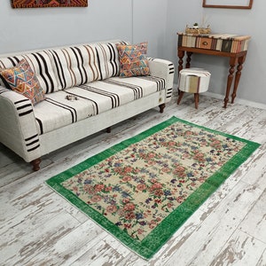 May include: A white and brown striped sofa with two pillows sits on a whitewashed wood floor. A green and cream floral rug with a green border is in front of the sofa.