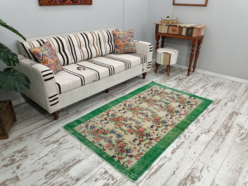 May include: A white and brown striped sofa with two pillows sits on a whitewashed wood floor. A green and cream floral rug with a green border is in front of the sofa.