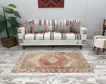 May include: A white and brown striped sofa with a white, cream, and pink patterned rug. The sofa has several colorful throw pillows with floral patterns.