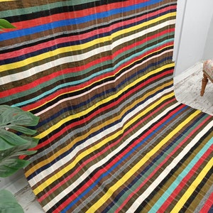 May include: A colorful striped rug with a variety of colors, including red, yellow, blue, green, and black. The rug is made of a woven fabric and has a fringed edge.