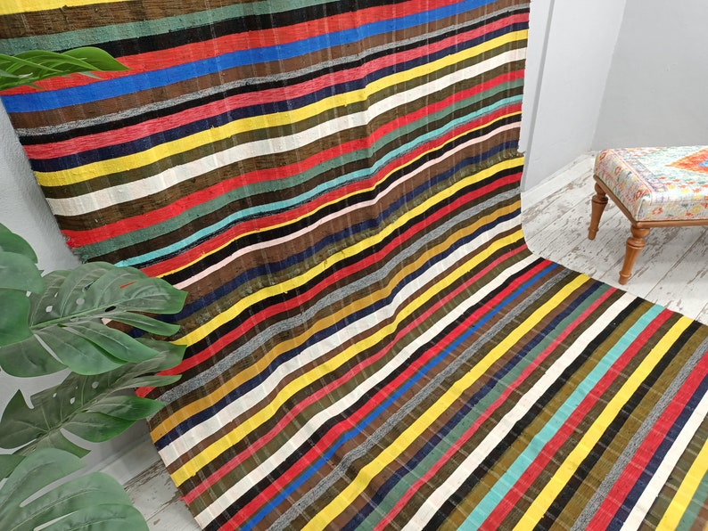 May include: A colorful striped rug with a variety of colors, including red, yellow, blue, green, and black. The rug is made of a woven fabric and has a fringed edge.