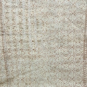 Puede incluir: Una alfombra blanca con un patr&oacute;n floral marr&oacute;n. La alfombra tiene un aspecto desgastado y est&aacute; hecha de un material suave y tejido.