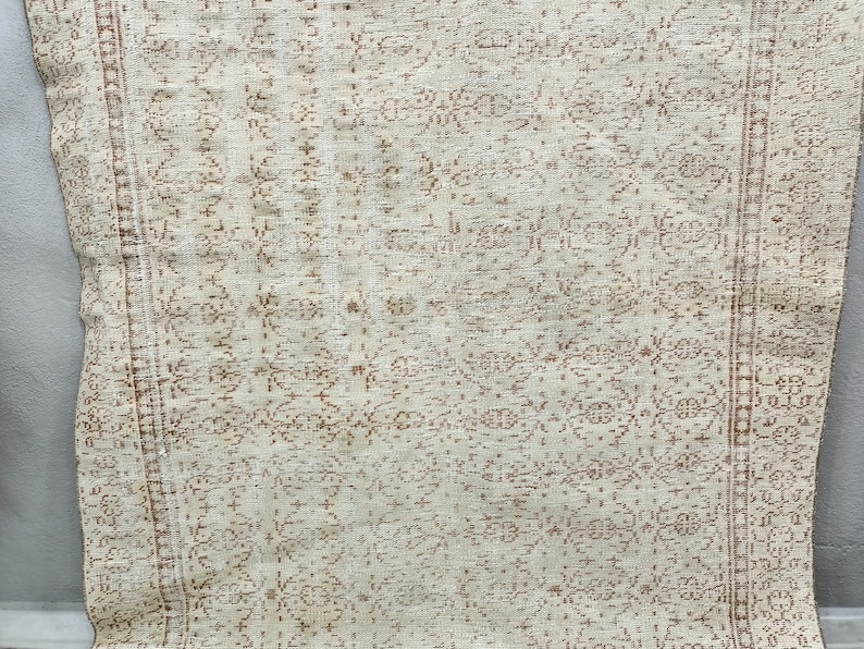 Puede incluir: Una alfombra blanca con un patr&oacute;n floral marr&oacute;n. La alfombra tiene un aspecto desgastado y est&aacute; hecha de un material suave y tejido.