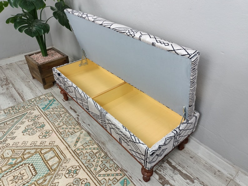 May include: A white and black patterned storage bench with a hinged lid open, revealing a yellow interior. The bench has wooden legs and is sitting on a light wood floor.