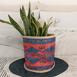 May include: A potted snake plant with green and yellow leaves in a colorful, patterned fabric planter. The planter has a blue, red, and pink geometric design.