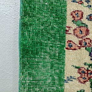 May include: Close-up of a green and cream rug with a floral pattern. The rug has a fringe border and is made of a soft, woven material.