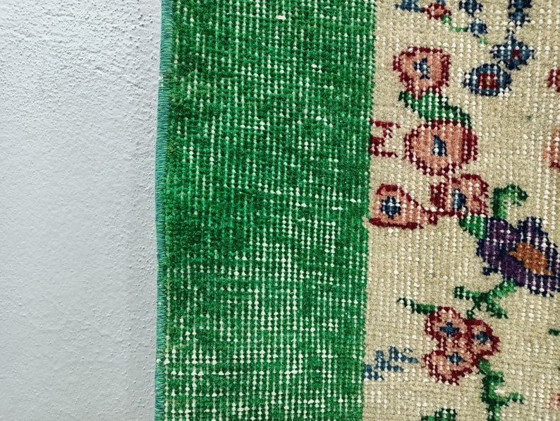 May include: Close-up of a green and cream rug with a floral pattern. The rug has a fringe border and is made of a soft, woven material.