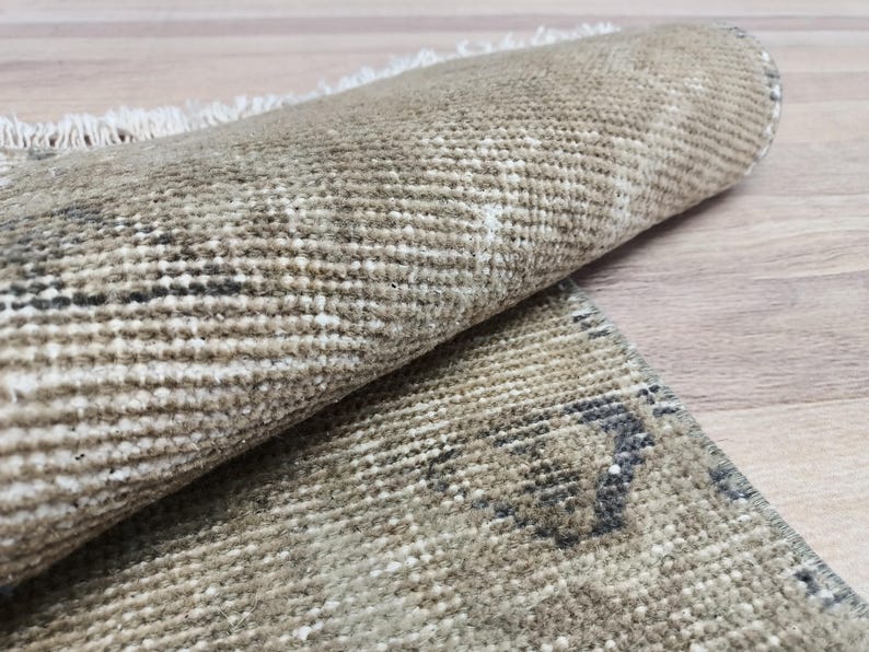 May include: A close-up of a beige and brown woven rug with a subtle pattern. The rug is rolled up, showing the texture of the weave.